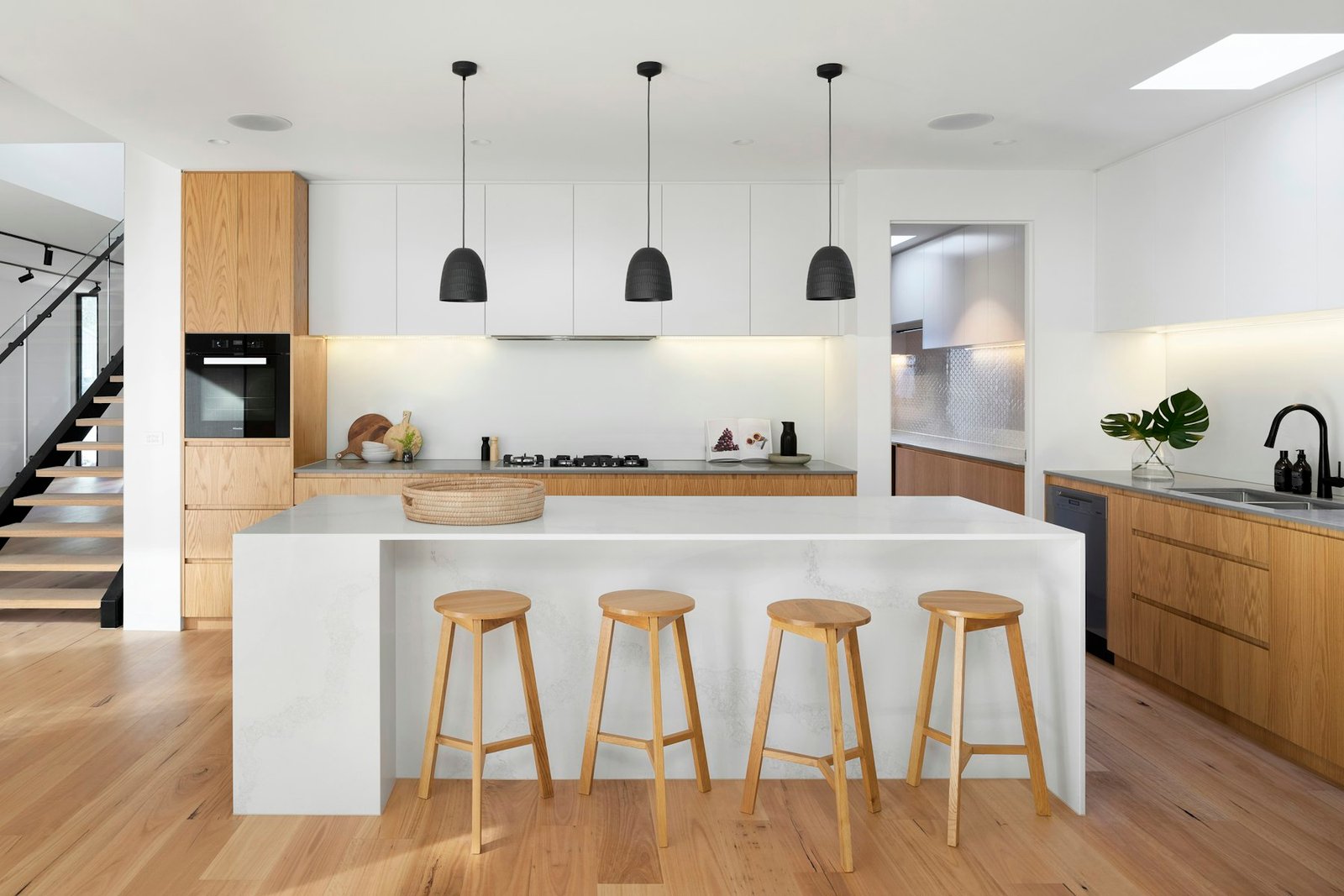 A handleless kitchen with a pale stone island, timber cabinetry and a row of stools.